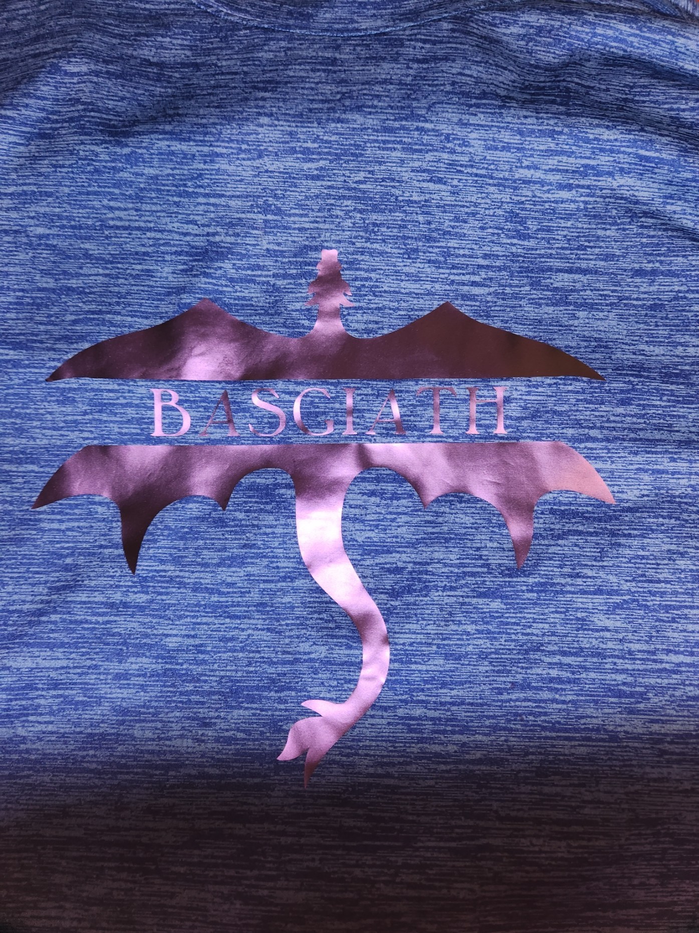 Blue shirt with an iridescent purple Basgiath wordmark inside a broad-winged dragon silhouette