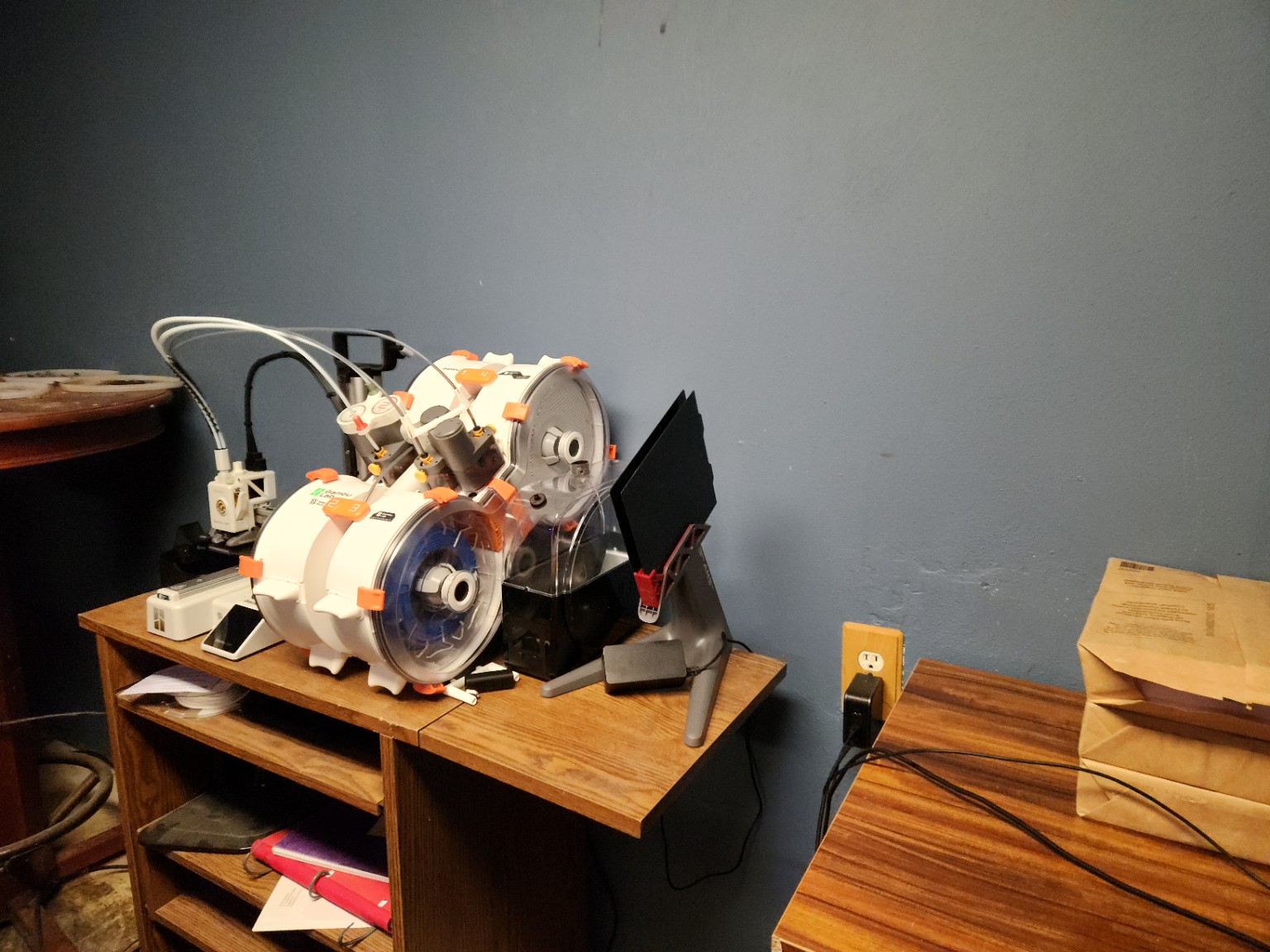 My filament-handling station with two enclosed filament spools feeding a compact 3D printer and a multispool stand beside the machine.