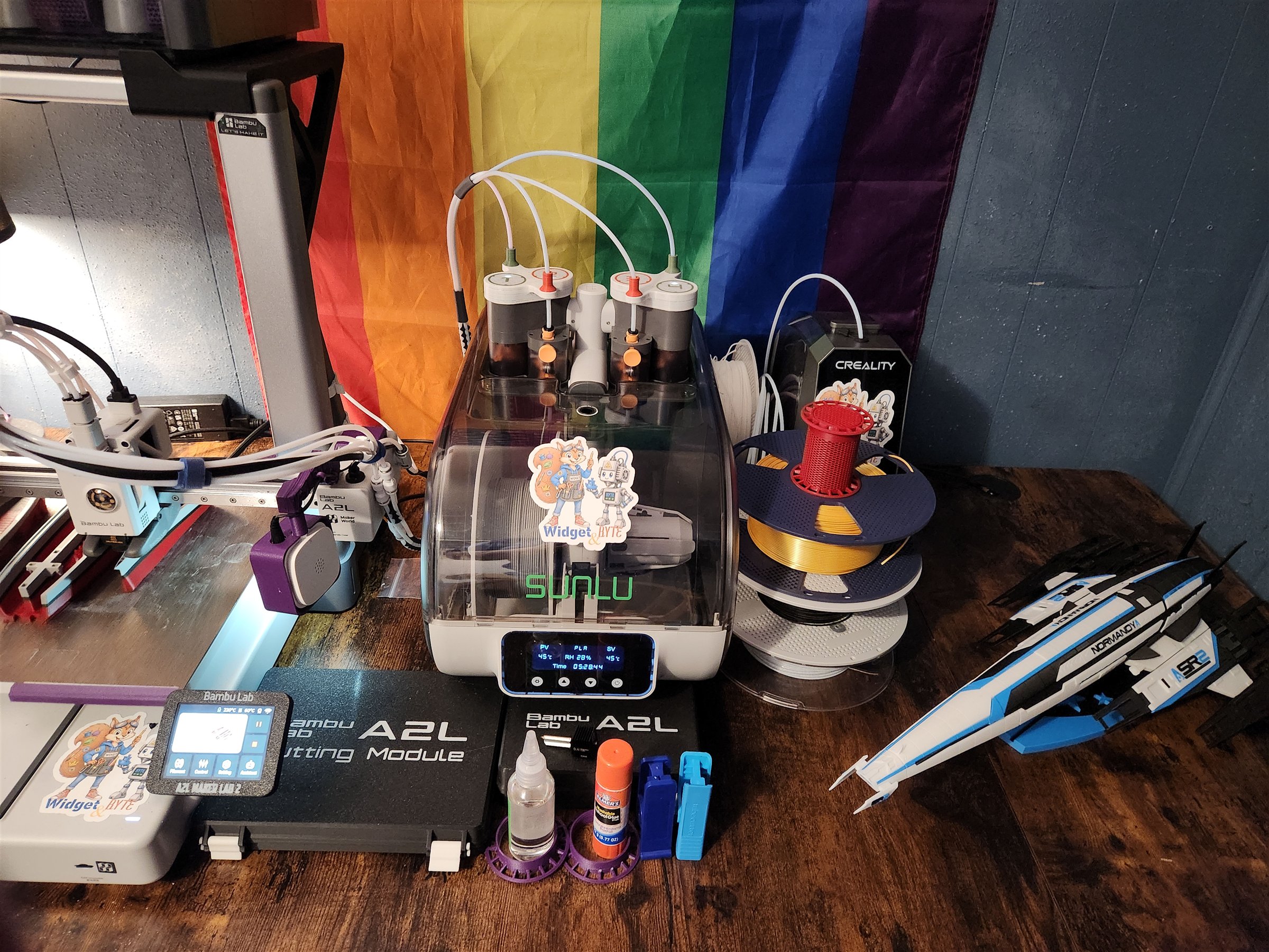 My Bambu Lab A2L workbench with a multispool filament system, SUNLU enclosure and dryer, stacked filament, a Creality dryer, tools, and a Normandy model